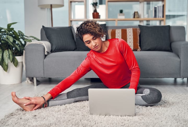 A woman stretching while looking at a laptop